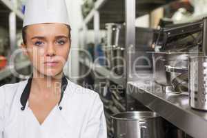 Young unsmiling chef standing arms crossed between shelves