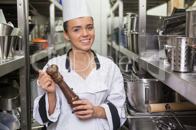 Young smiling chef holding pepper mill between shelves