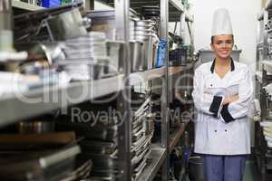 Young happy chef standing arms crossed between shelves
