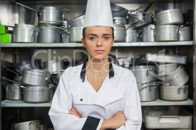 Young content chef standing arms crossed between shelves