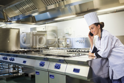 Young happy chef standing next to work surface phoning