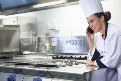 Young smiling chef standing next to work surface phoning