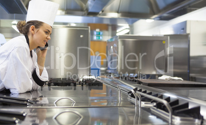 Young pretty chef standing next to work surface phoning