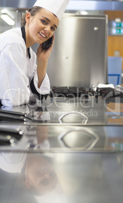 Young cheerful chef standing next to work surface phoning