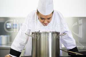 Young pretty chef looking into saucepan