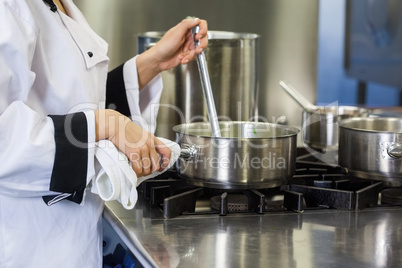 Young chef stirring with ladle holding pot