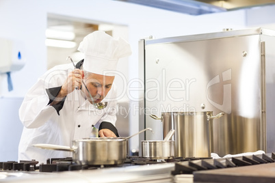 Focused head chef tasting food from ladle