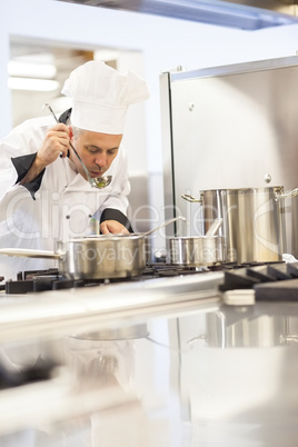 Concentrating head chef tasting food from ladle