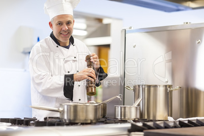 Smiling head chef flavoring food with pepper