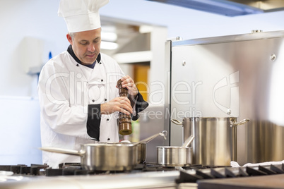 Focused head chef flavoring food with pepper