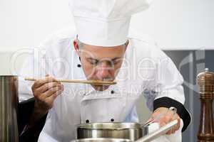 Focused head chef tasting sauce with wooden spoon