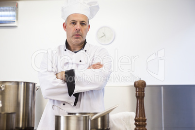 Serious head chef standing arms crossed behind pot