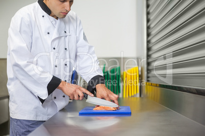 Chef cutting raw salmon with knife on blue cutting board