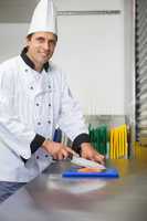 Smiling chef cutting raw salmon with knife on blue cutting board