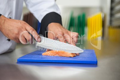 Chef slicing raw salmon with knife on blue cutting board
