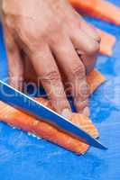 Close up of hand slicing salmon with sharp knife