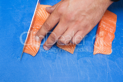 Close up of hand slicing raw salmon with sharp knife