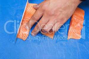 Close up of hand slicing raw salmon with sharp knife