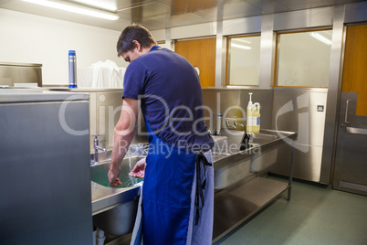 Kitchen porter washing up at sink