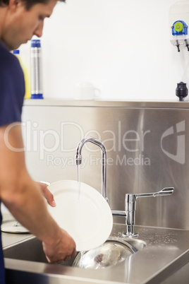 Kitchen porter cleaning plates in sink