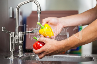 Kitchen porter washing pepper under running tap