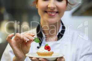 Smiling head chef putting mint leaf on little cake on plate