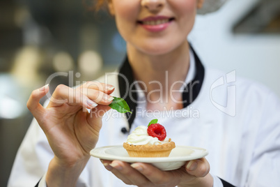 Happy head chef putting mint leaf on little cake on plate