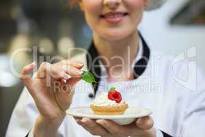 Happy head chef putting mint leaf on little cake on plate