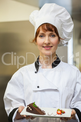 Pretty smiling chef presenting chocolate cake with strawberries