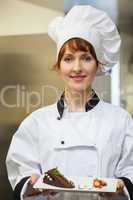 Pretty smiling chef presenting chocolate cake with strawberries