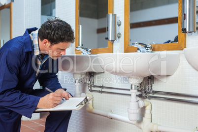 Handsome plumber looking at sink holding clipboard