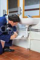 Handsome plumber inspecting sink holding clipboard
