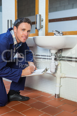Smiling plumber inspecting sink holding clipboard