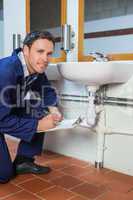 Smiling plumber inspecting sink holding clipboard