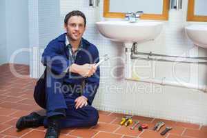 Handsome smiling plumber sitting next to sink holding wrench