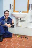 Handsome cheerful plumber sitting next to sink showing thumb up
