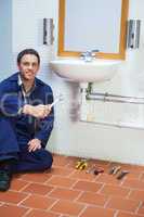 Handsome cheerful plumber sitting next to sink holding wrench