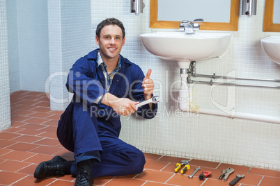 Handsome happy plumber sitting next to sink showing thumb up