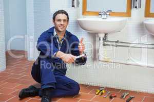 Handsome happy plumber sitting next to sink showing thumb up