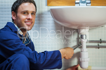 Handsome smiling plumber repairing sink