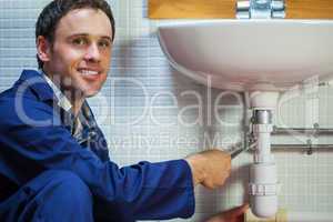 Handsome smiling plumber repairing sink