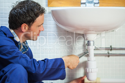 Handsome happy plumber repairing sink