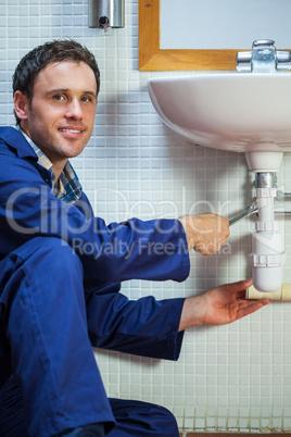 Handsome cheerful plumber repairing sink