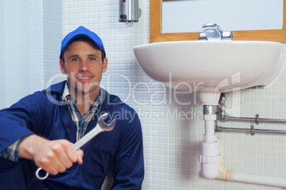 Smiling plumber holding wrench sitting next to sink