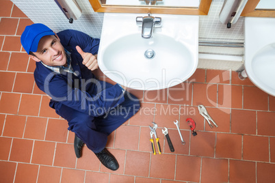 Cheerful plumber repairing sink showing thumb up