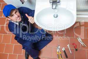 Smiling plumber repairing sink showing thumb up