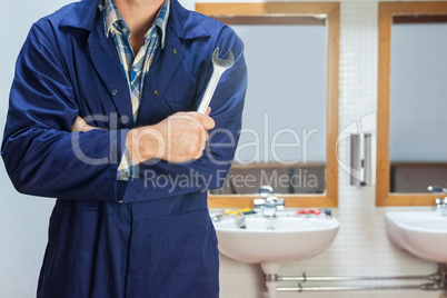 Plumber in blue boiler suit posing with wrench