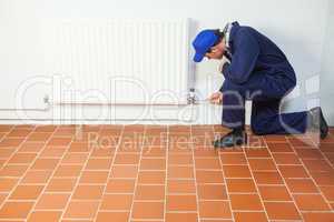 Handyman in blue boiler suit repairing a radiator