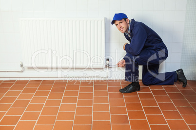 Handyman in blue boiler suit repairing a radiator smiling at cam