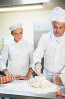 Serious head chef showing trainee how to prepare dough